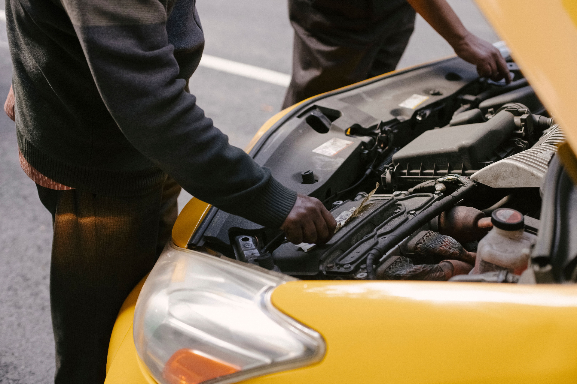 Mechanic inspecting the engine bay of a yellow car after an accident for damage assessment and repair estimate in Cape Town